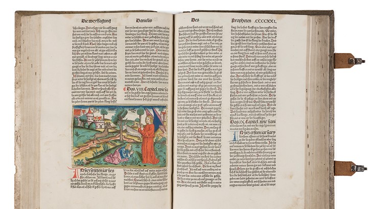 Medieval bible open at pages showing a colour illustration and printed text in Latin